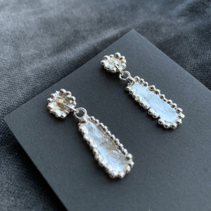 silver oblong stud drop earrings shown on a black earring card with a grey velvet background