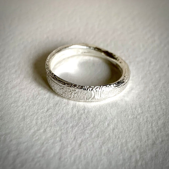 A single solid silver D shaped textured band ring