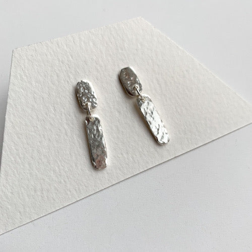 Short Silver Hammer textured rectangular tab shaped drop earrings displayed on an earring card